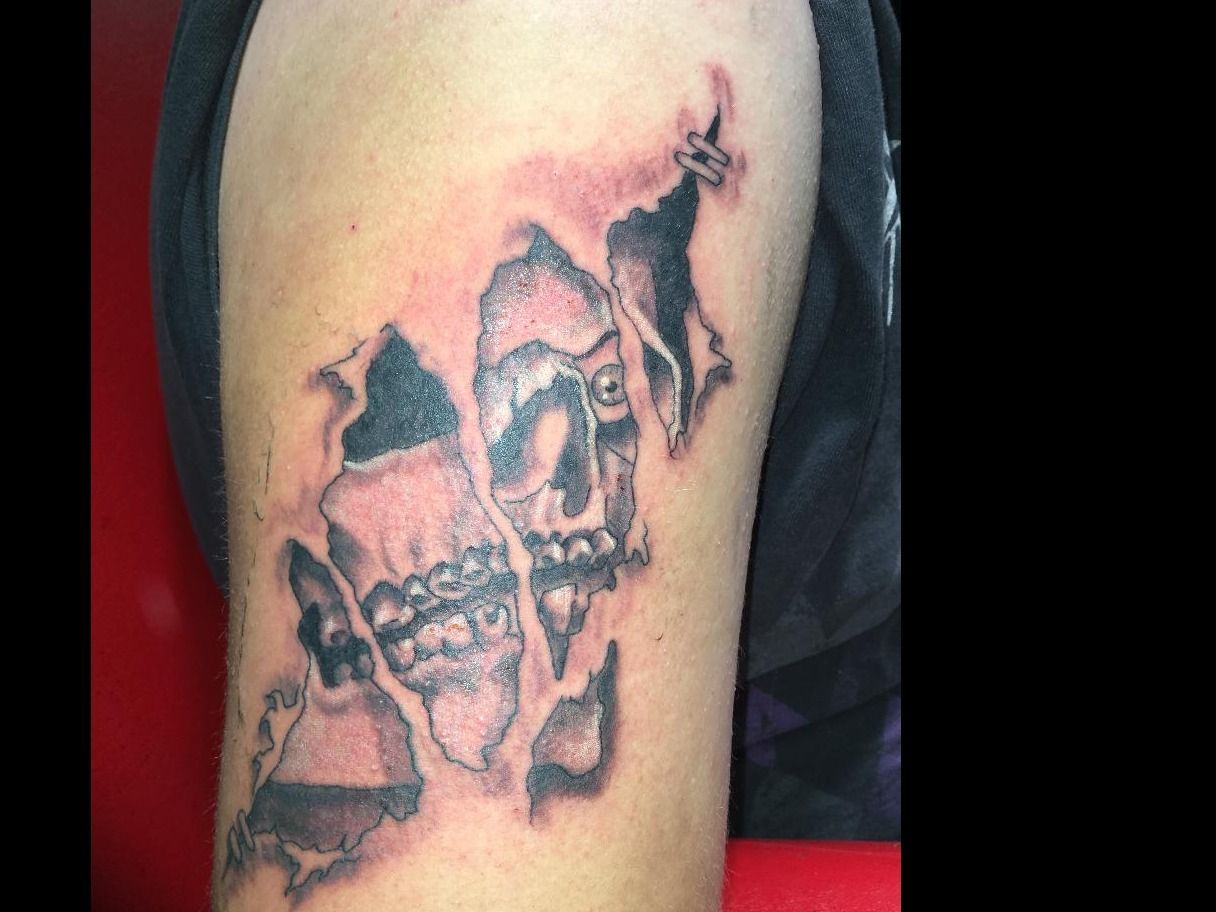 A man has a tattoo of a skull with braces on his arm.