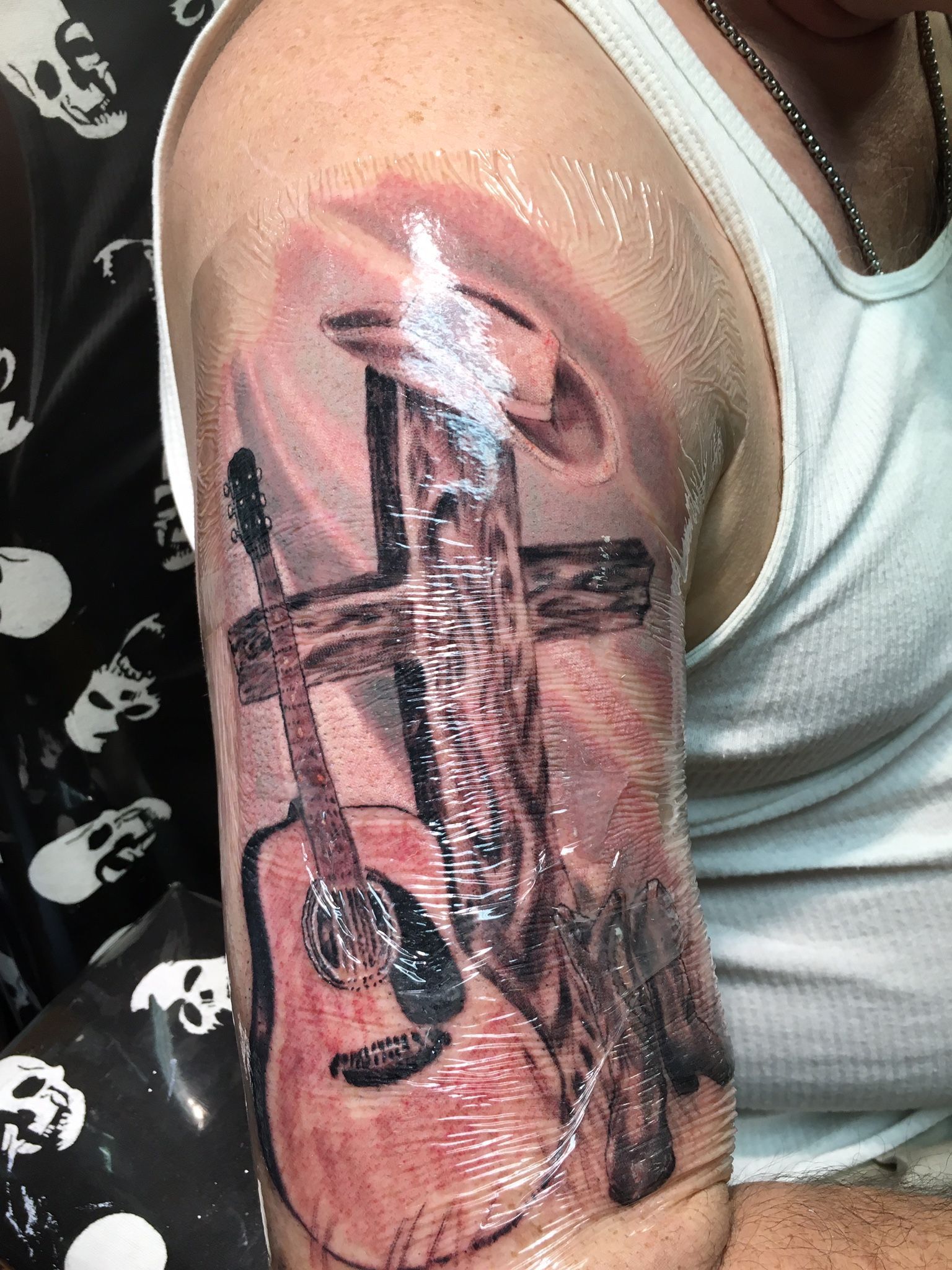 A man has a tattoo of a guitar and a cross on his arm.