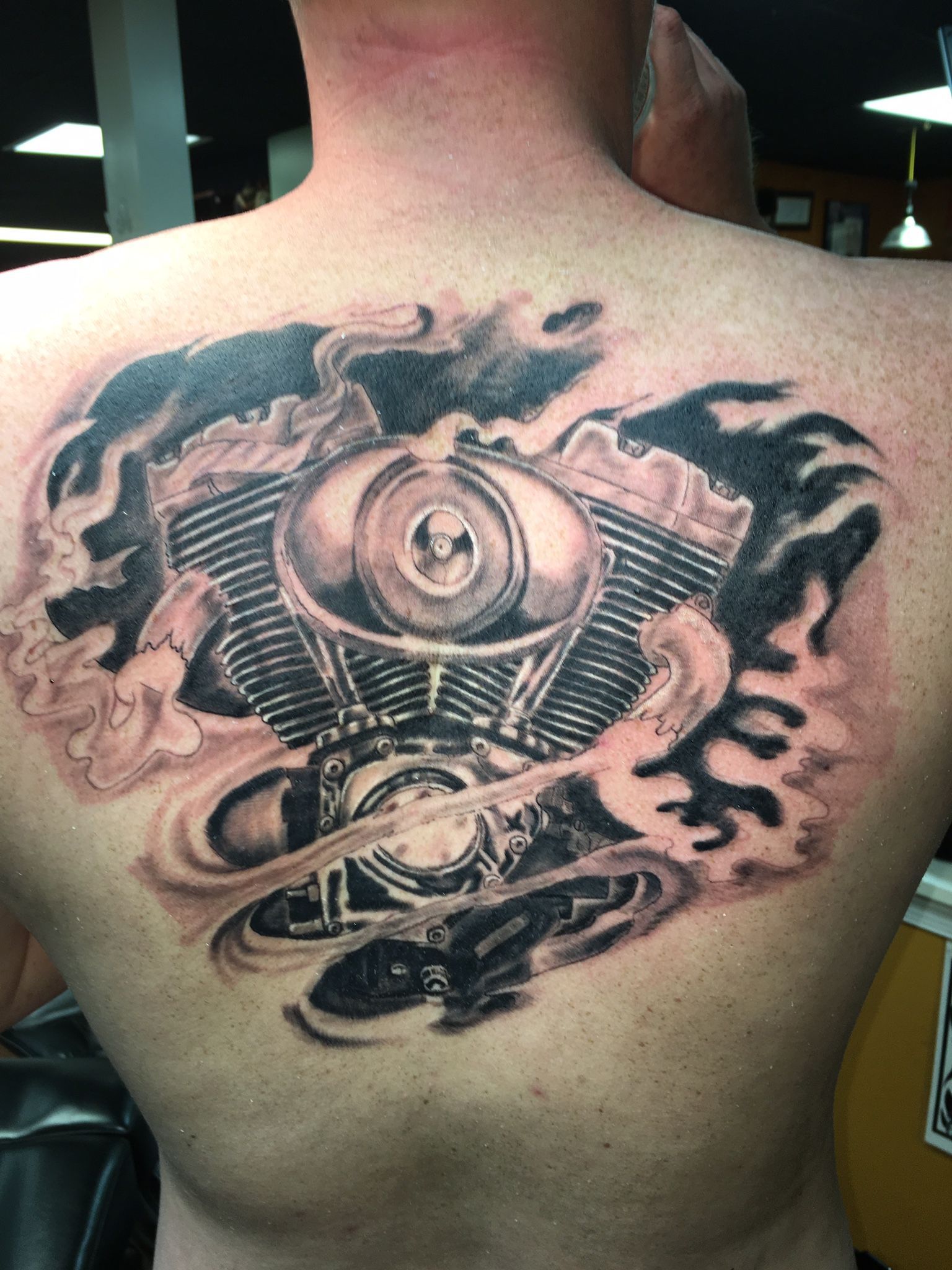 A man has a tattoo of a motorcycle engine on his back.