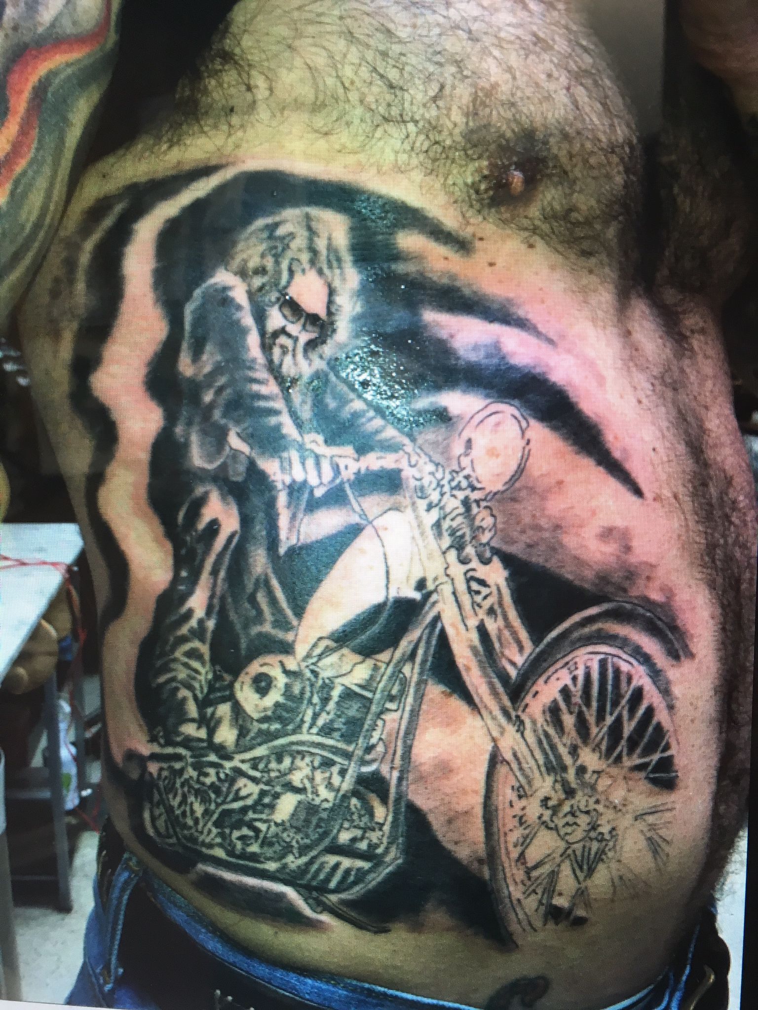 A man has a tattoo of a grim reaper riding a motorcycle
