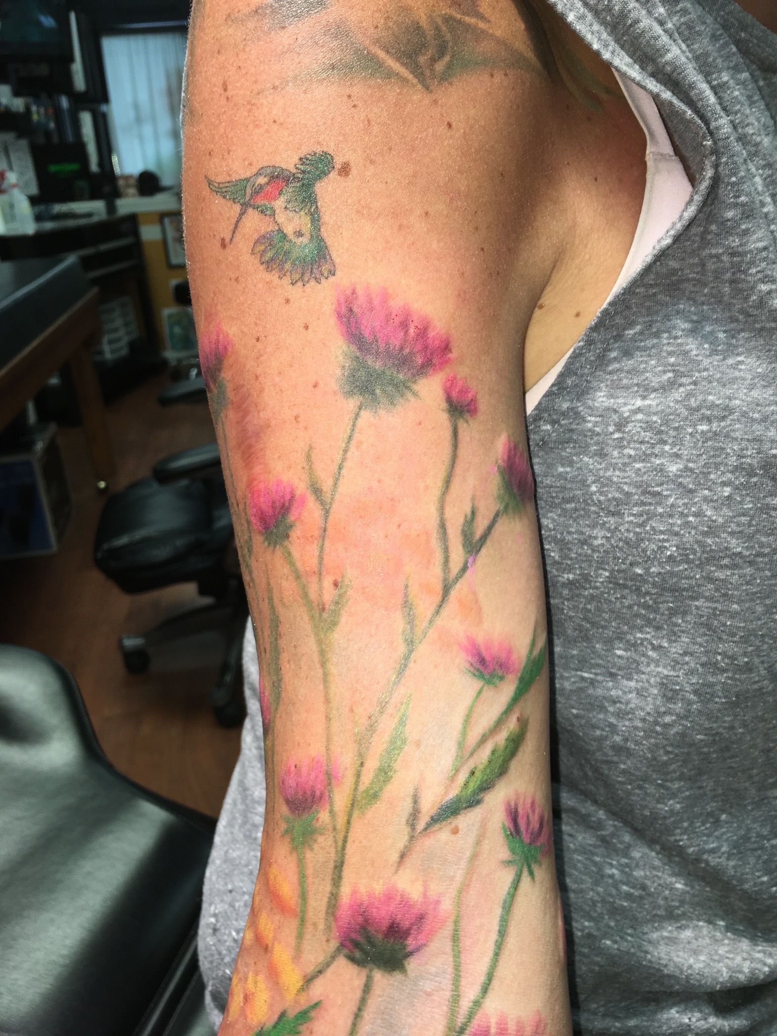 A woman has a tattoo of flowers and a hummingbird on her arm.