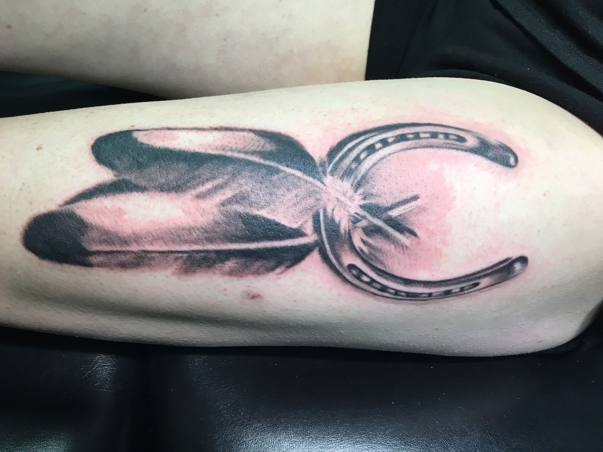 A person has a tattoo of a horseshoe and feather on their arm