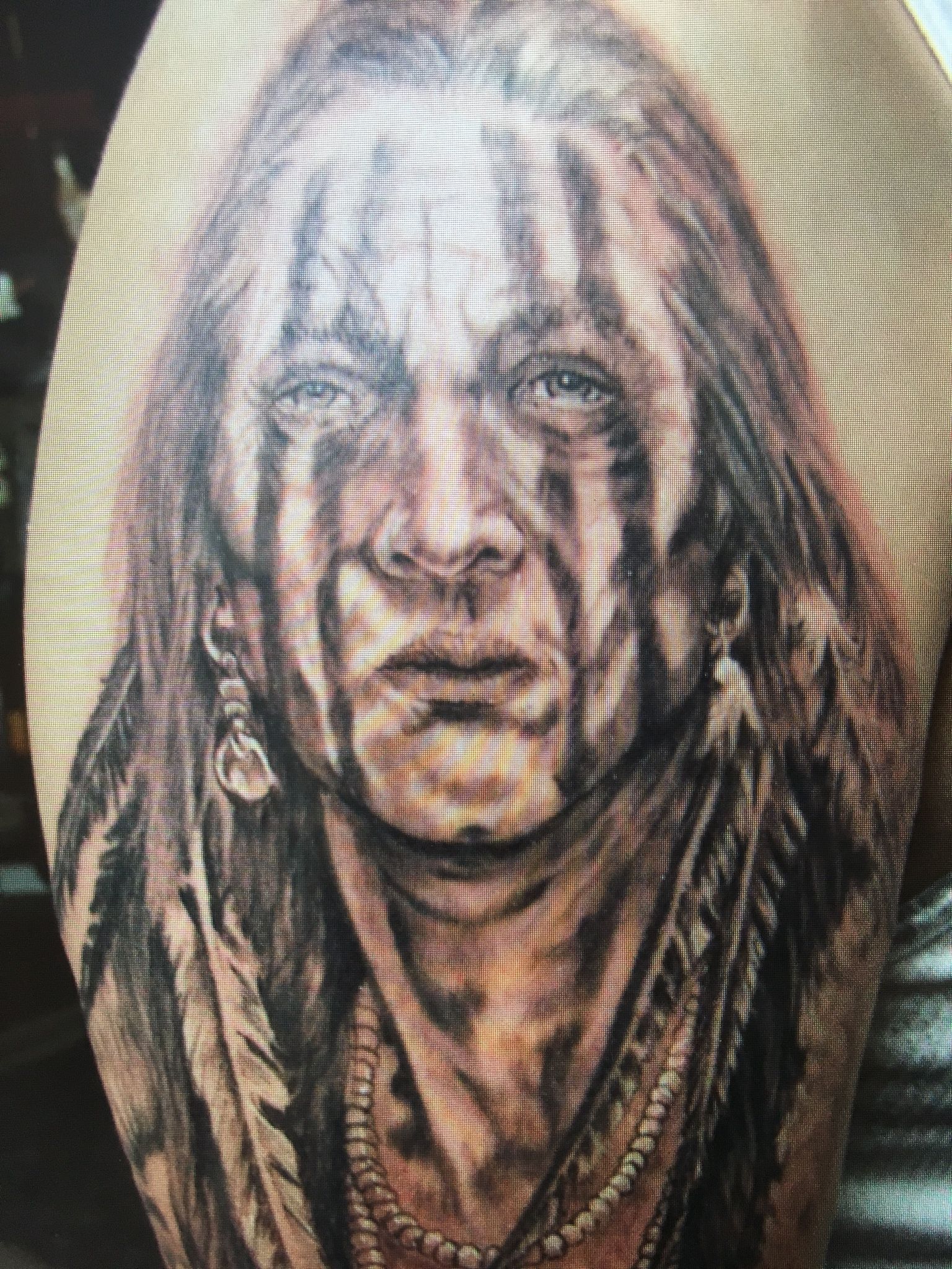 A black and white tattoo of a native american with feathers on his head.