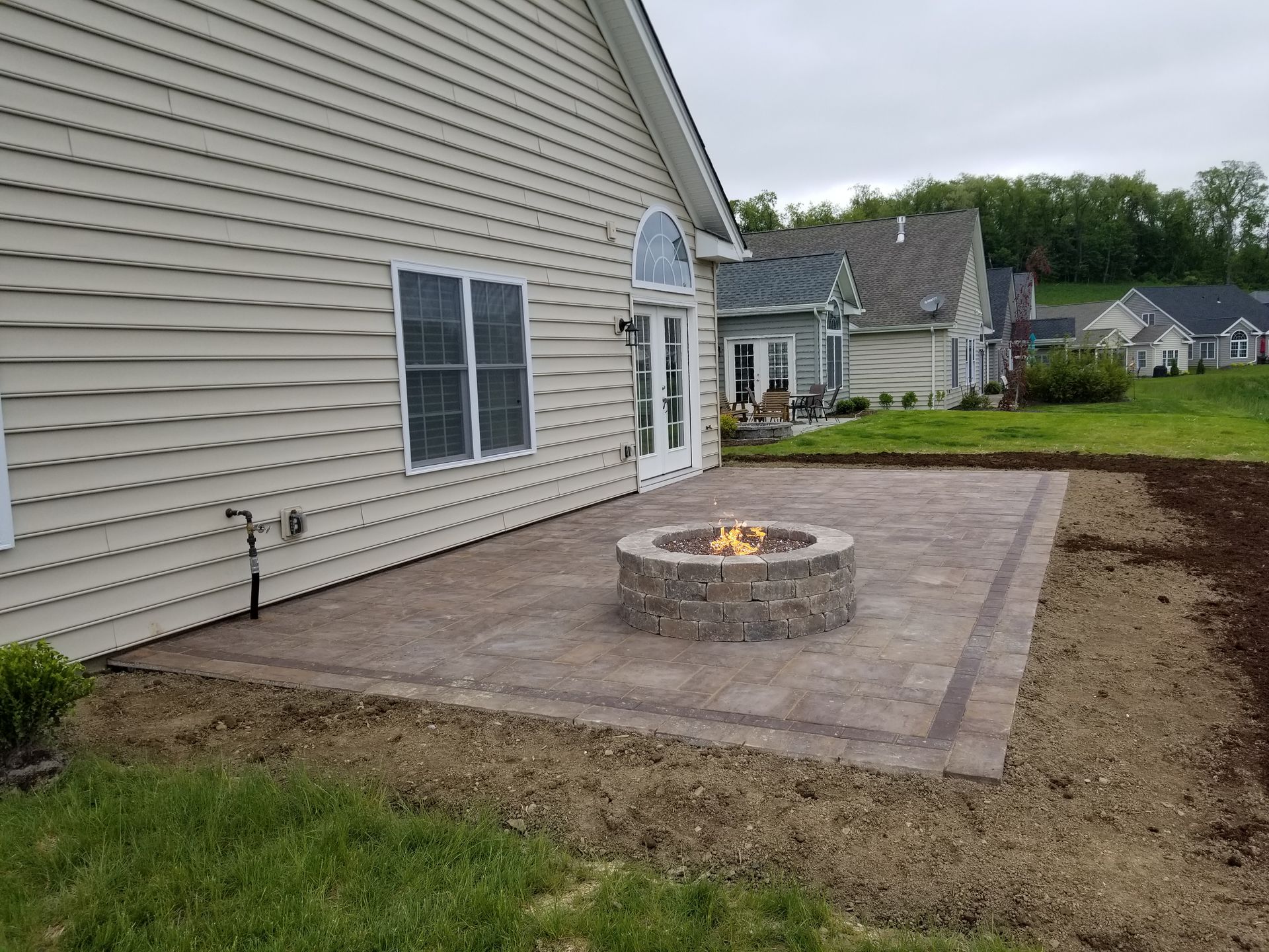 Backyard patio with a stone fire pit beside a beige house and neighboring homes.
