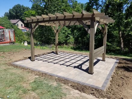 Wooden pergola on a concrete pad with a trellis floor in a wooded backyard area