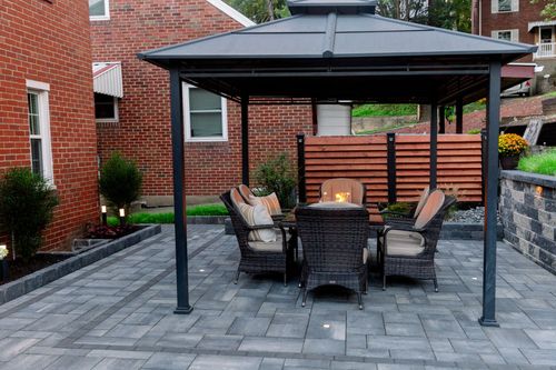 Covered patio with outdoor seating, fire pit, and gray pavers beside a brick house.