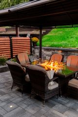 Outdoor patio with wicker chairs around a fire pit under a covered pergola at dusk
