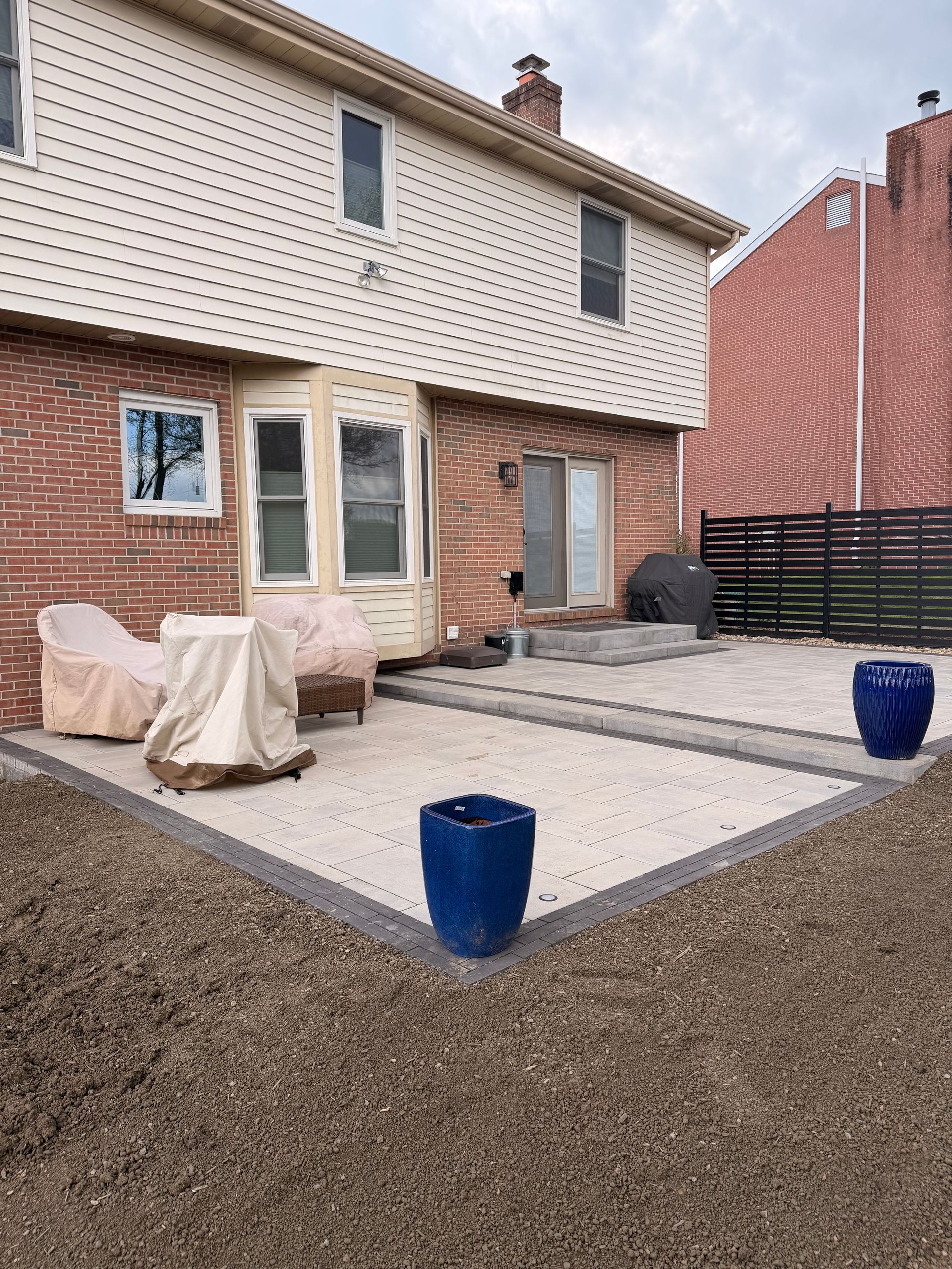 Backyard patio with a house, gravel ground, blue planters, and covered furniture.