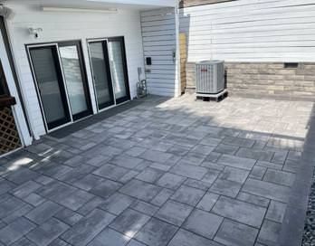 Patio with gray pavers, sliding glass doors, and an outdoor air-conditioning unit by a white house.