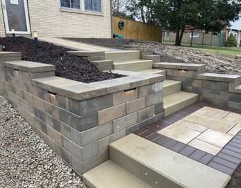 Stone retaining walls and concrete steps leading up to a house with a small paved patio.