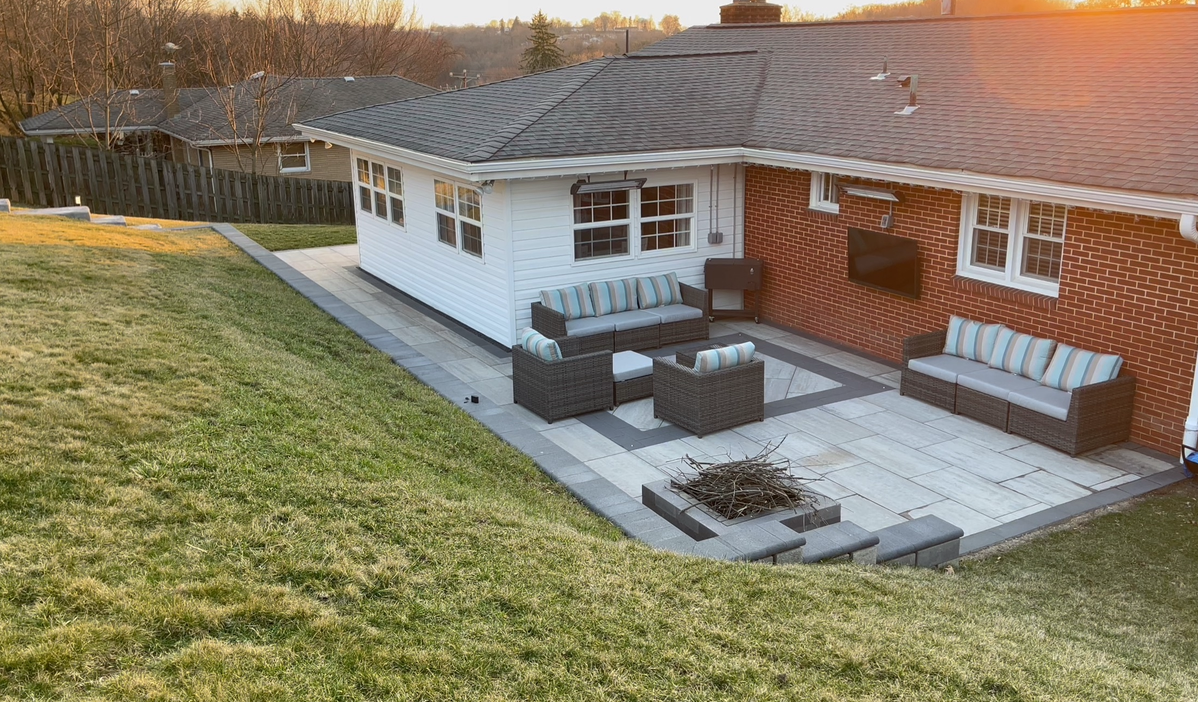 Backyard patio with outdoor seating beside a white house and sloped grass lawn.