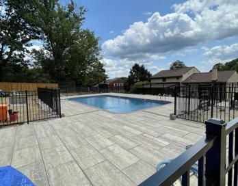 Outdoor swimming pool with gray deck, black railings, and cloudy sky