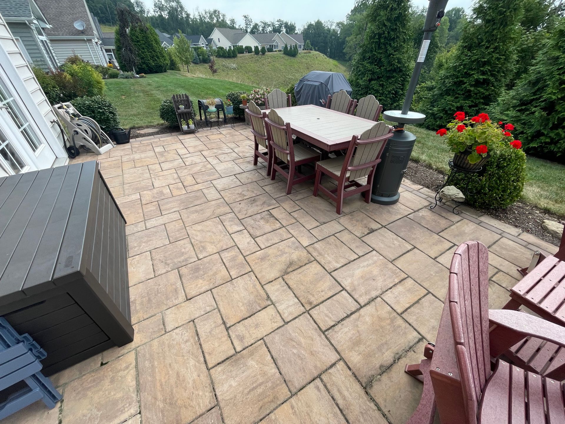 Patio with outdoor dining table, chairs, grill, and flower pots overlooking a grassy backyard.