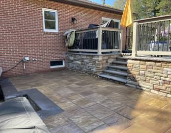 Brick patio with stone steps, raised deck, patio furniture, and a closed yellow umbrella.