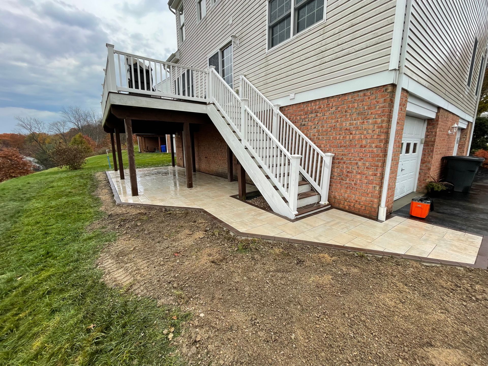 White staircase and raised deck attached to a house beside a concrete patio and grassy yard.