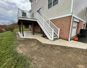 Backyard deck with white stairs, brick siding, and a concrete patio area next to a grassy yard