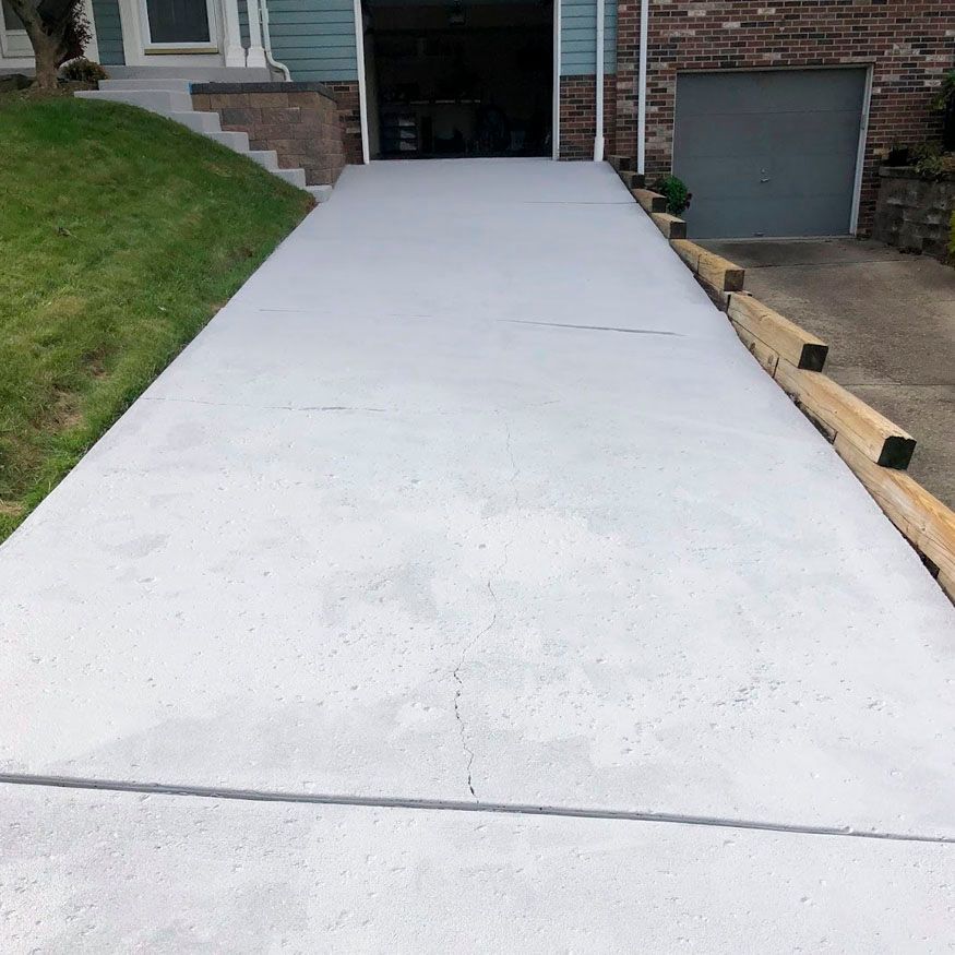 Concrete driveway leading to a brick garage, with grassy slopes on both sides.