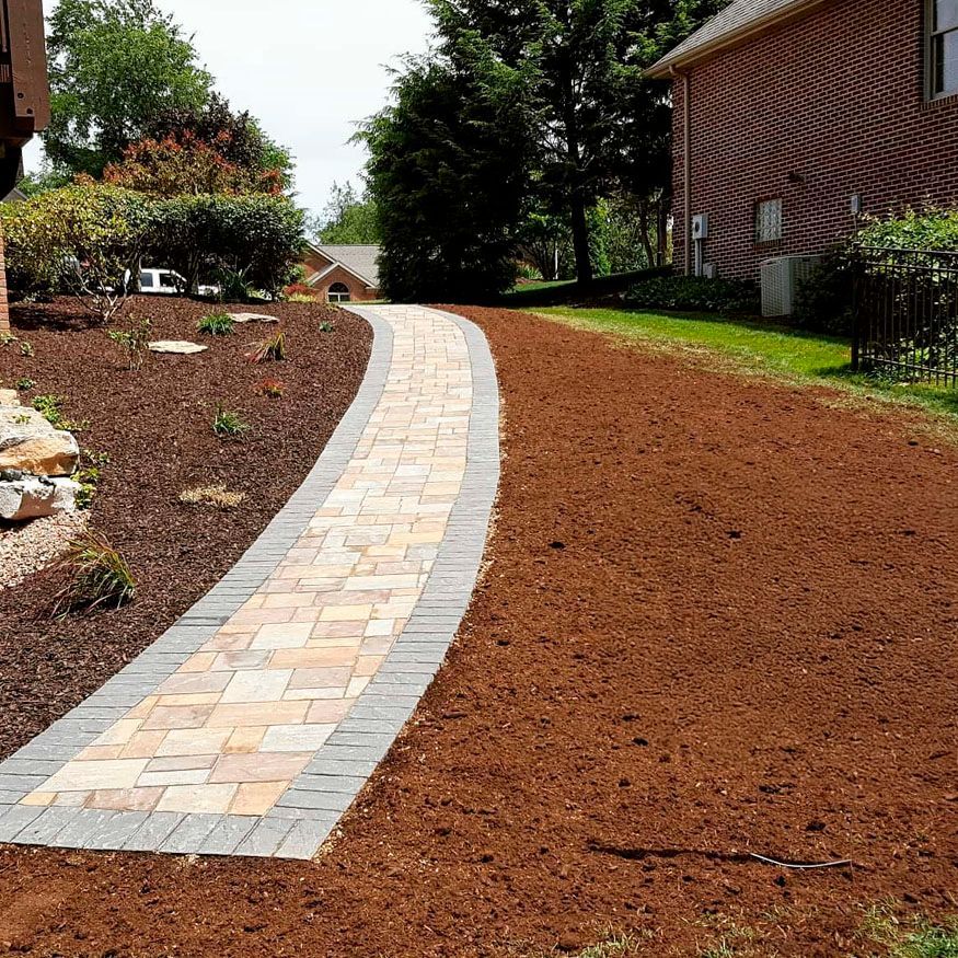 Curved stone walkway through a mulched garden beside a brick house