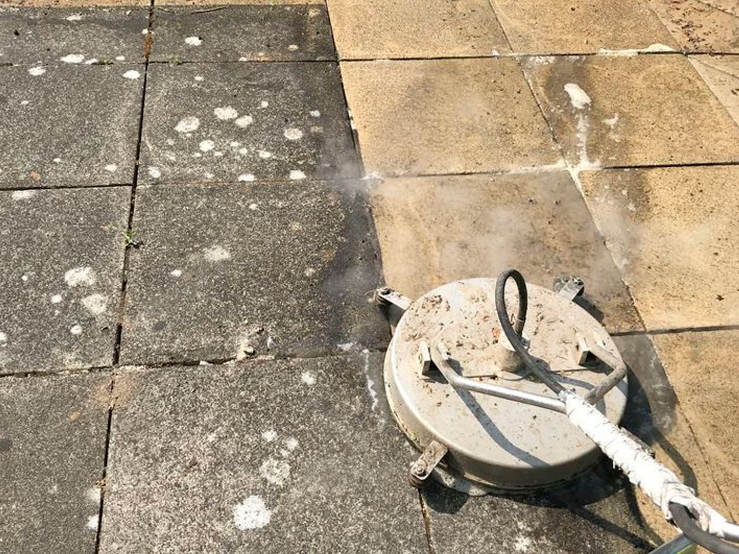 Round metal manhole cover on a tiled pavement with a white hose or cable attached.