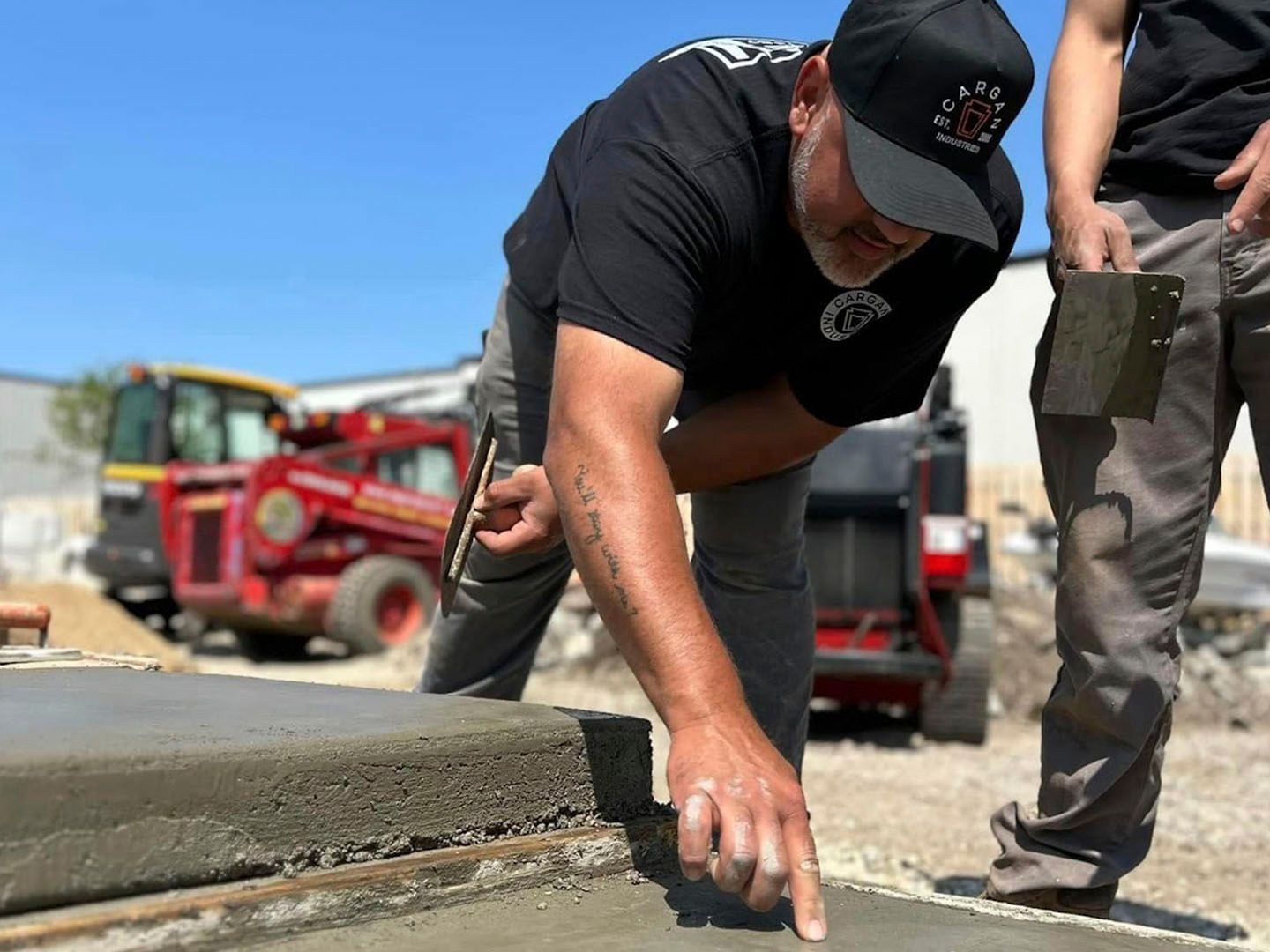 Construction worker smoothing fresh concrete at a roadside worksite with a trowel.