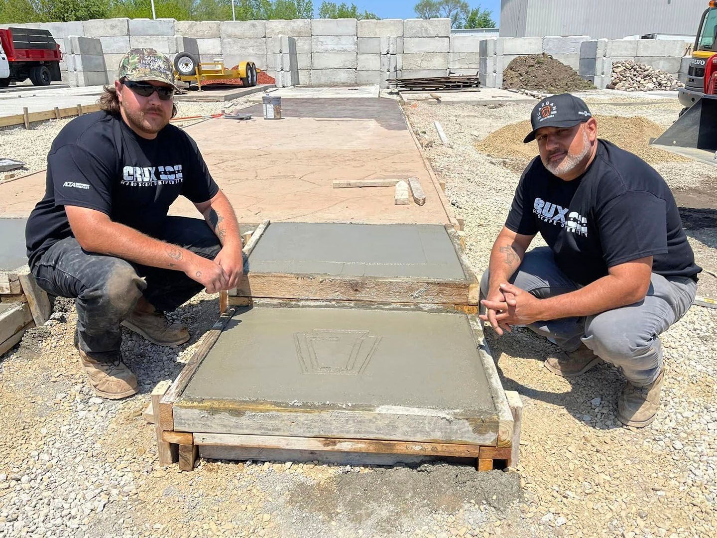 Two workers kneel beside a freshly poured concrete slab at a construction site.