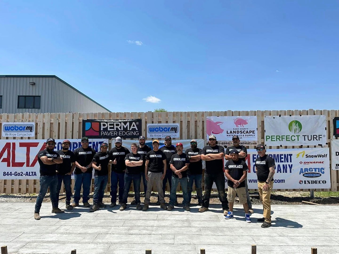 Group of people standing in front of sponsor banners at an outdoor event, posing for a photo