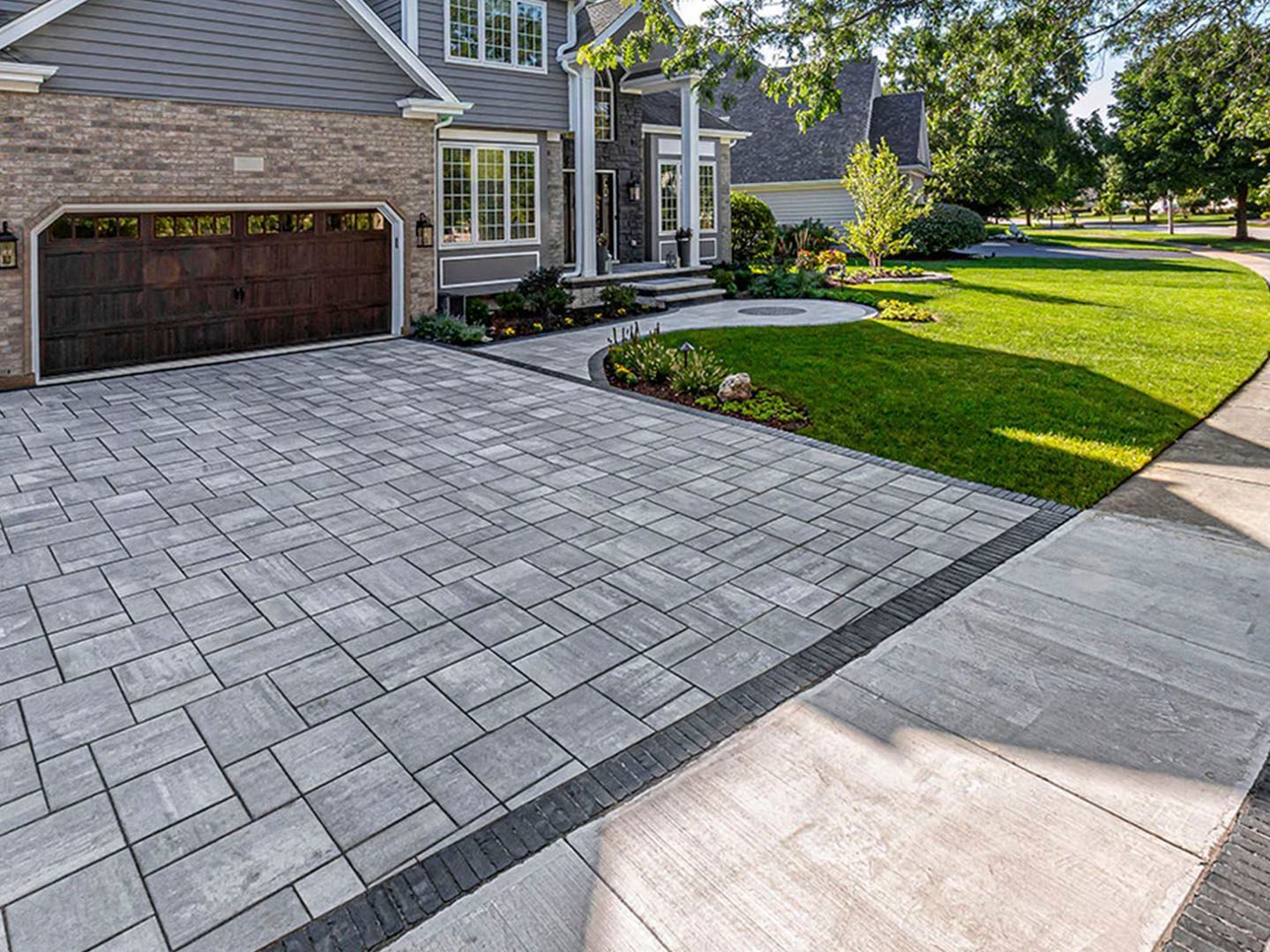 Suburban house with brick driveway, garage, green lawn, and sidewalk in front