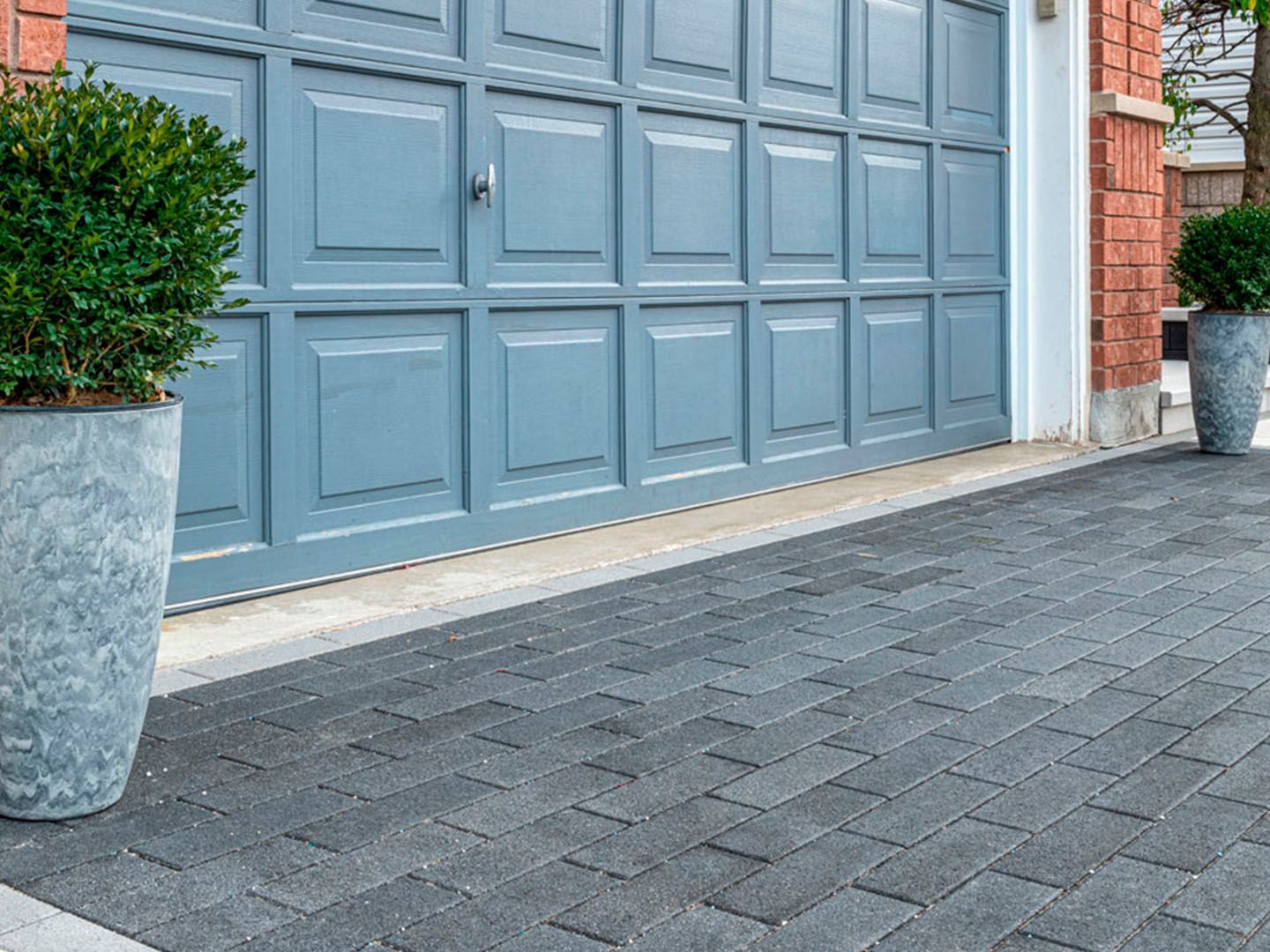 Blue garage door beside gray paver driveway and potted plants