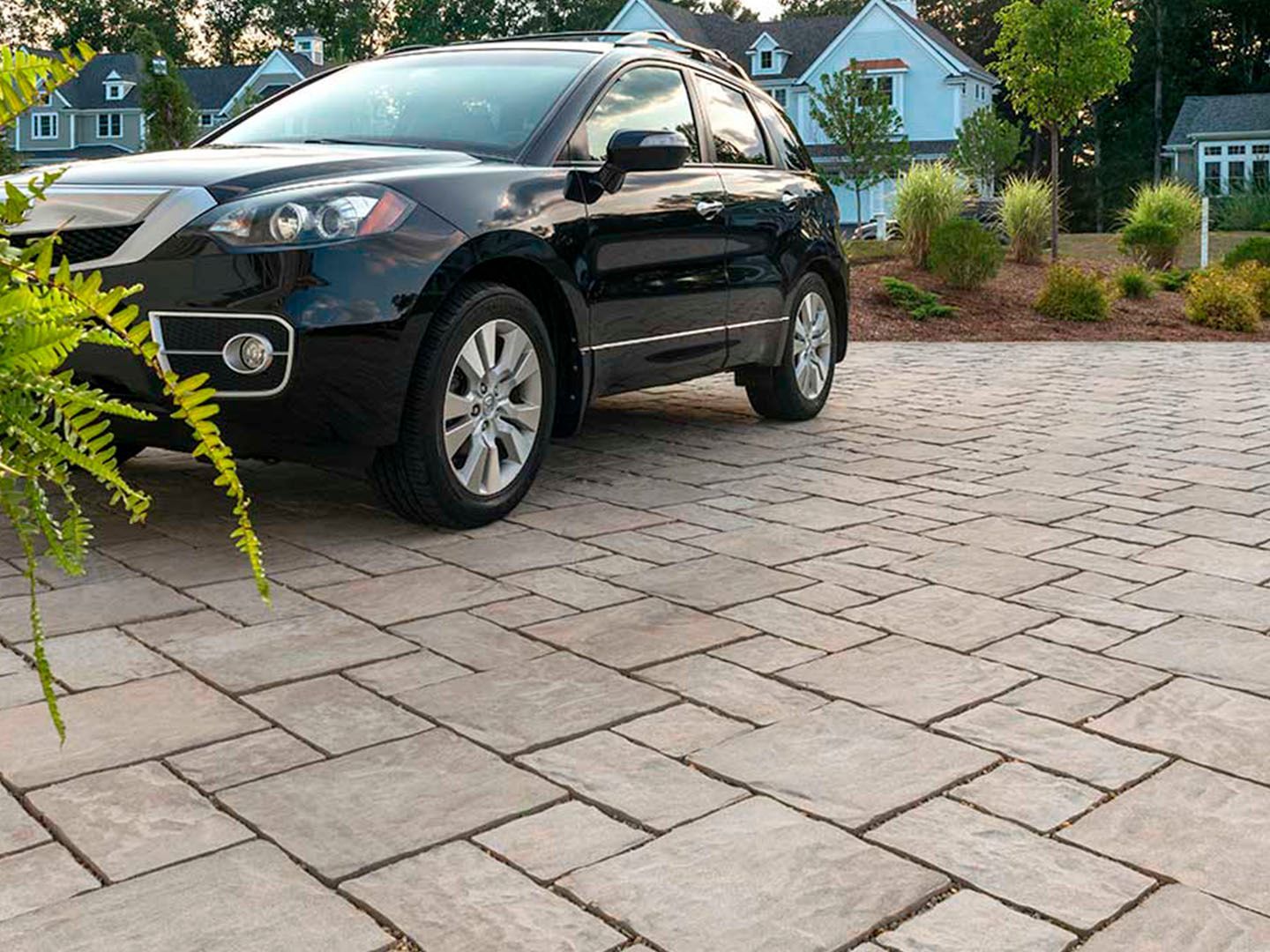 Black SUV parked on a brick driveway in front of blue houses and green shrubs
