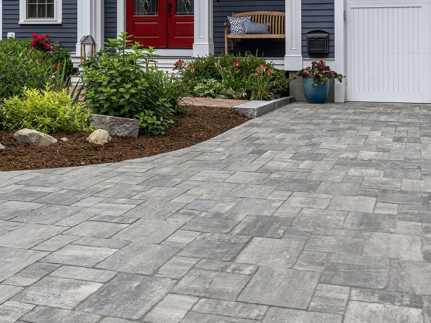 Gray stone driveway beside a front garden and house with red door and white garage