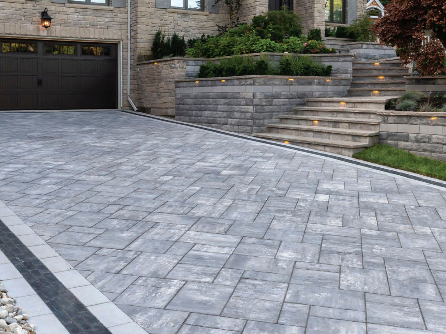 Stone driveway leading to a garage and landscaped front steps beside a stone house
