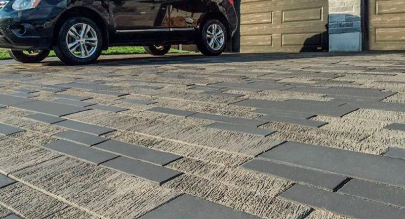 Paved driveway with gray rectangular pavers, viewed low angle, with a black car parked in front of a garage.
