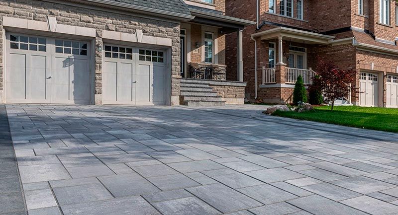 Residential driveway with gray pavers leading to a garage and brick house entry