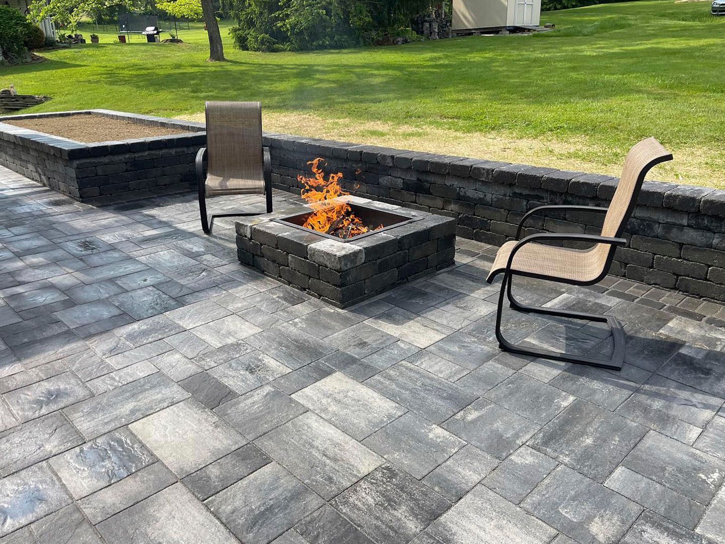 Patio with stone fire pit, two outdoor chairs, and a grassy backyard beyond.