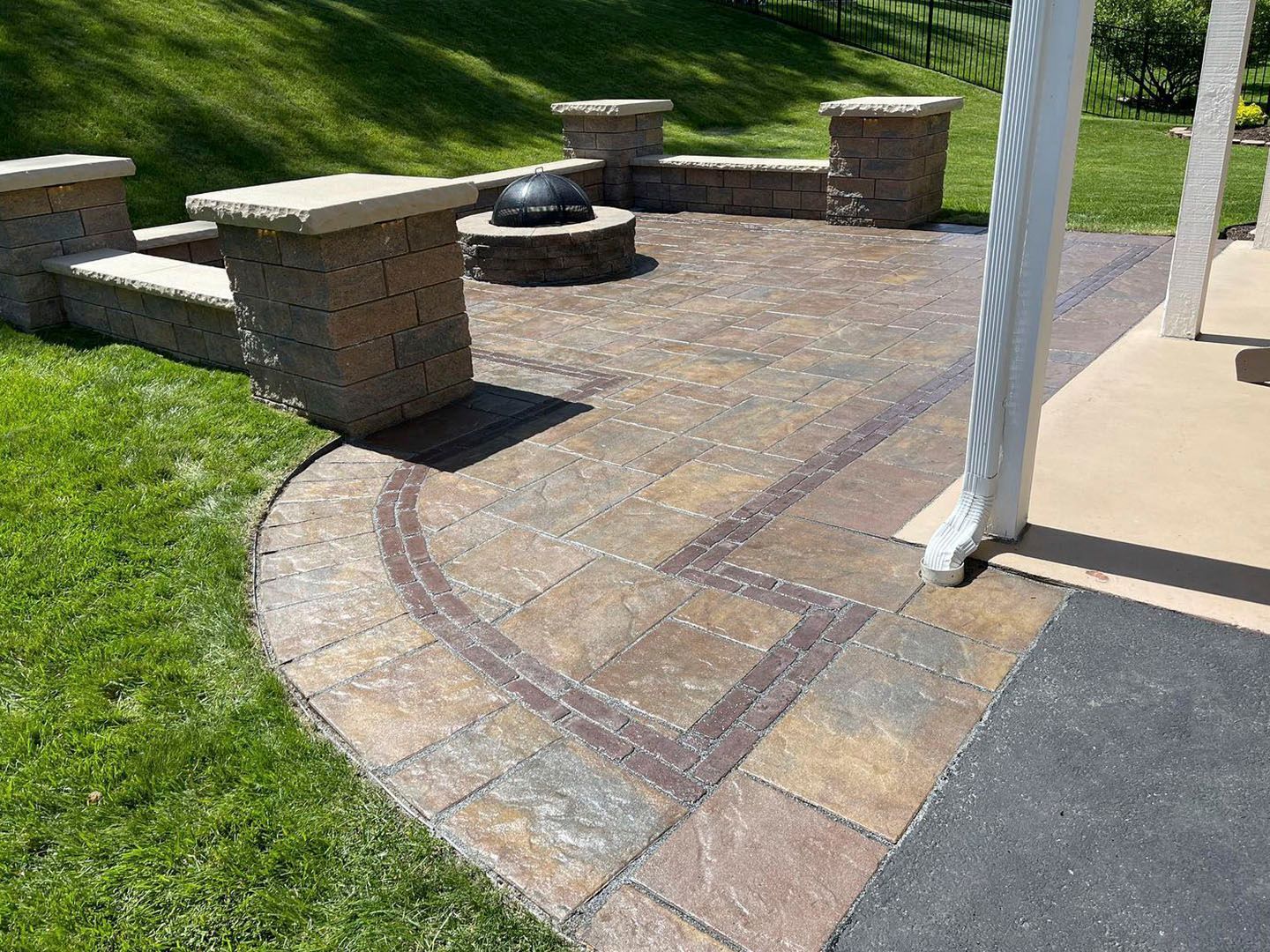 Curved brick patio with low stone benches and a black fire pit beside a grassy lawn