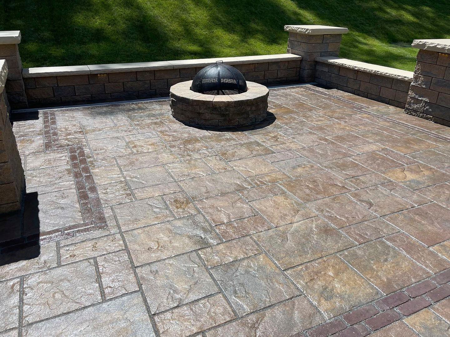 Stone patio with a circular fire pit and low stone wall overlooking grass