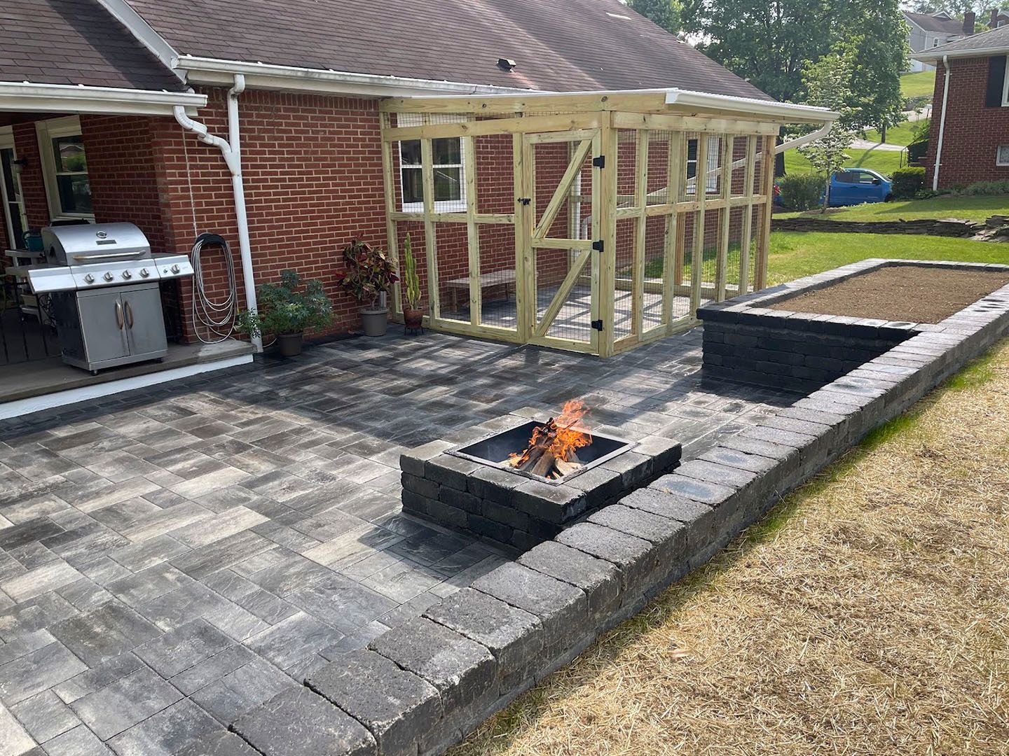 Backyard patio with fire pit, grill, raised planters, and a wooden pergola beside a brick house
