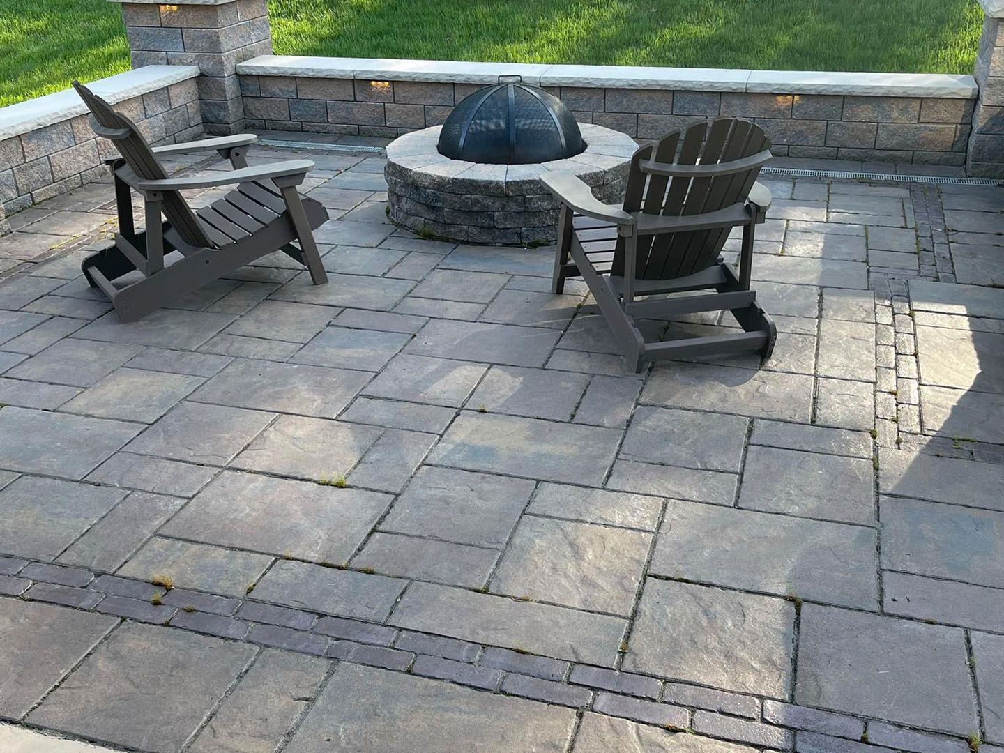 Stone patio with two wooden chairs around a fire pit beside a grassy yard