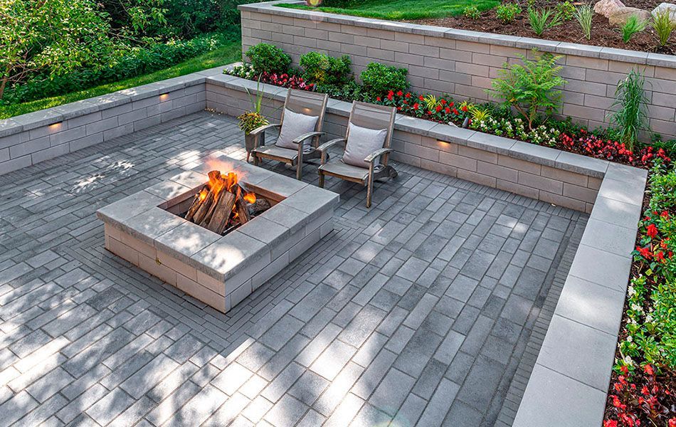 Modern patio with a square fire pit, four chairs, and paver seating area bordered by flowers