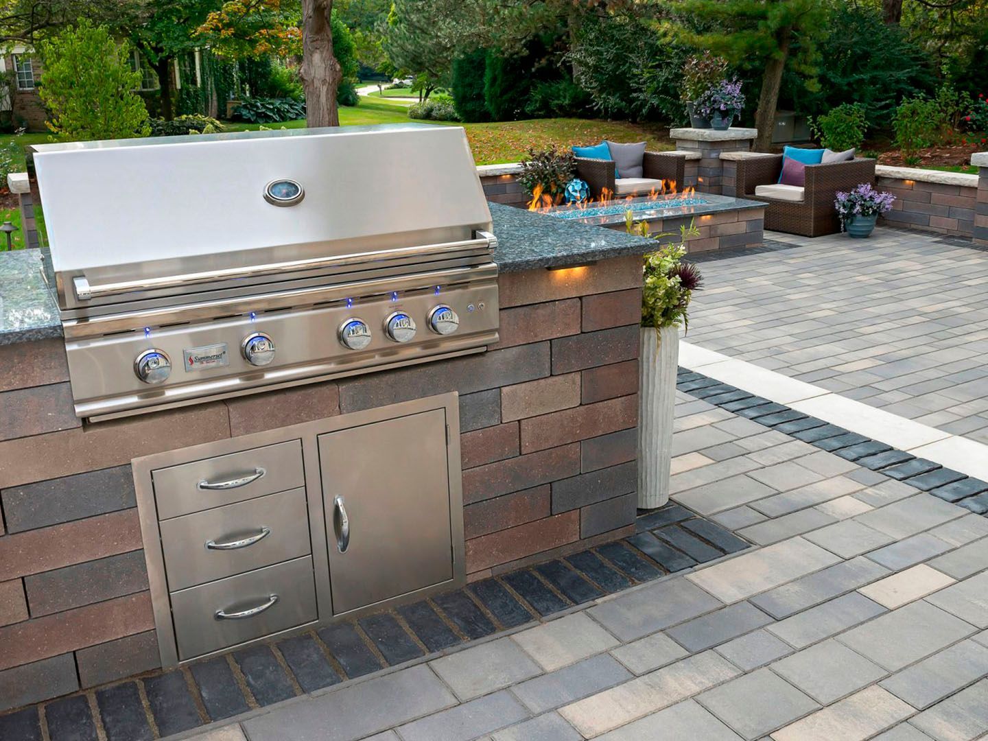 Outdoor stainless steel grill and brick island on a patio with paver flooring and garden seating area