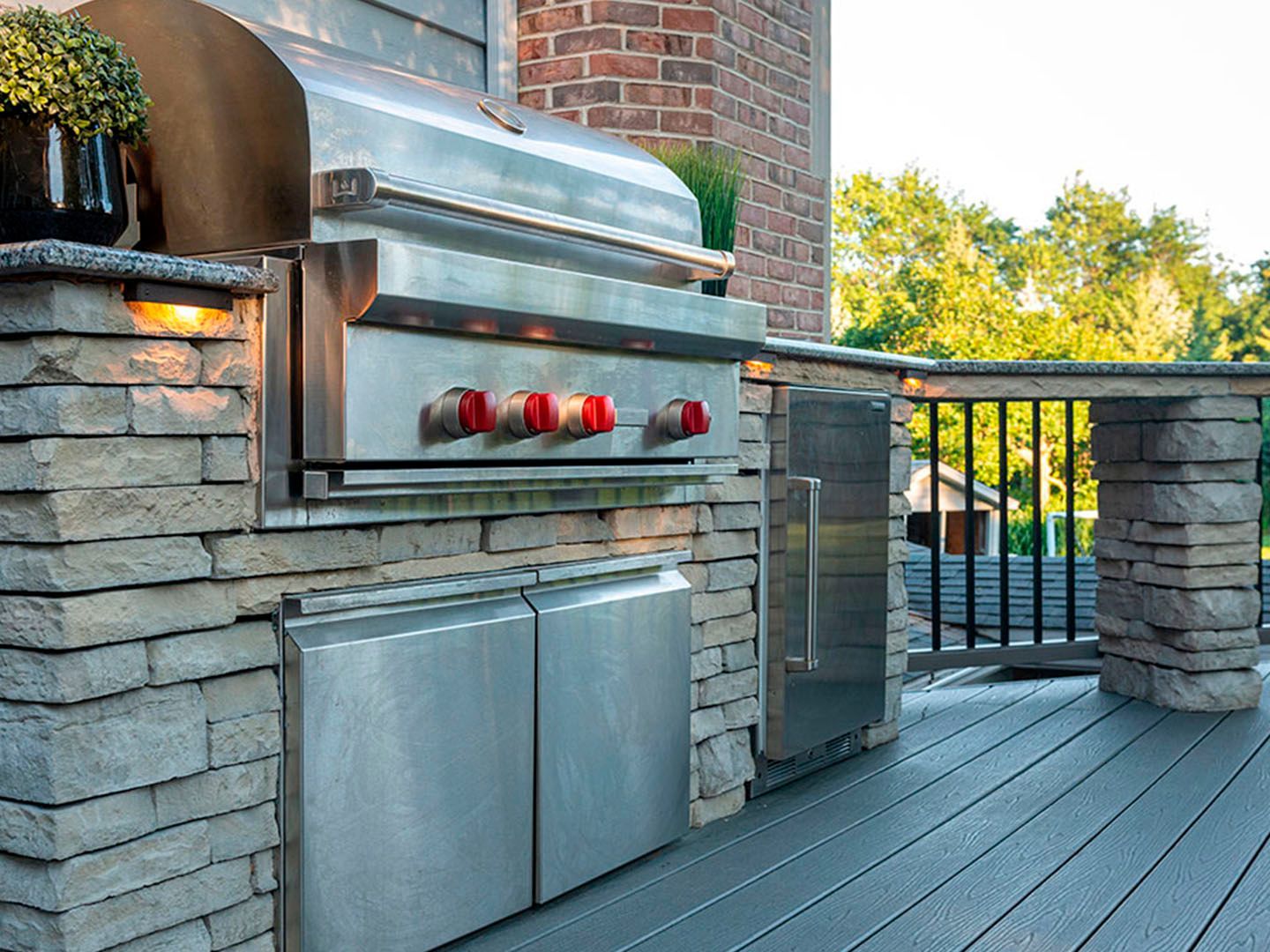 Built-in stainless steel outdoor grill on a stone patio with wooden decking and black railing