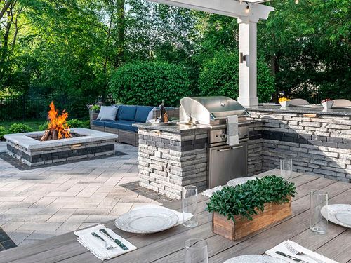 Backyard patio with stone fire pit, grill, and outdoor seating under a white pergola