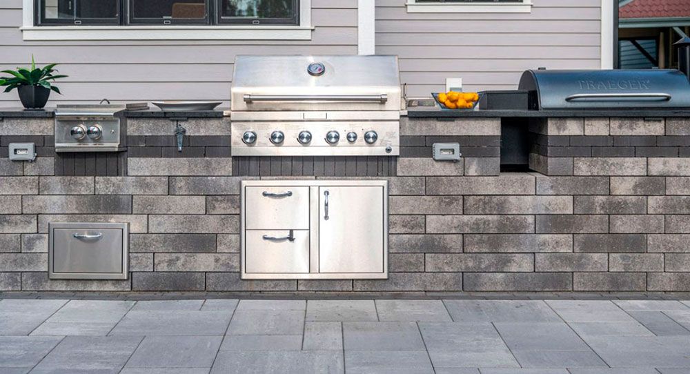 Outdoor built-in stainless steel grill and cabinet setup against a stone wall on a patio