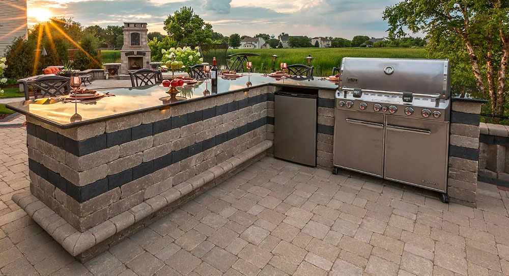 Outdoor patio with a built-in grill, stone counter, and sunset view over a green landscape