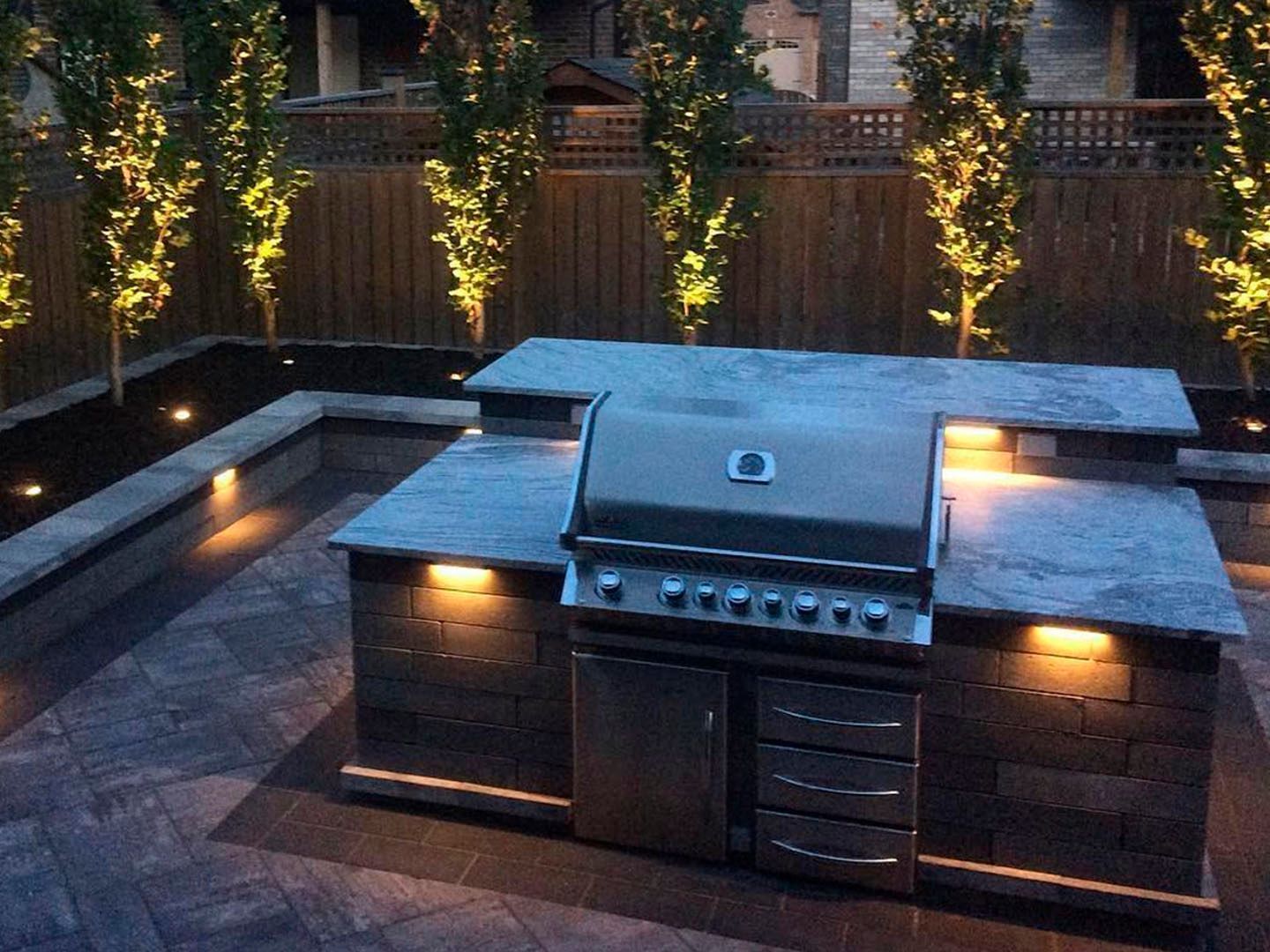 Outdoor patio with built-in grill and warm landscape lighting at dusk