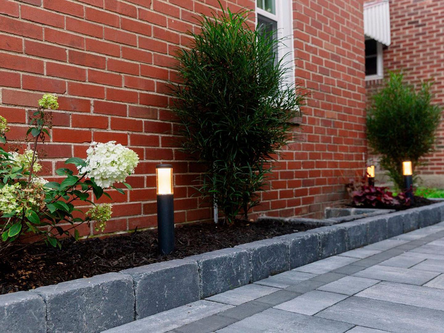 Brick building with landscaped shrubs and path lights along a paved walkway