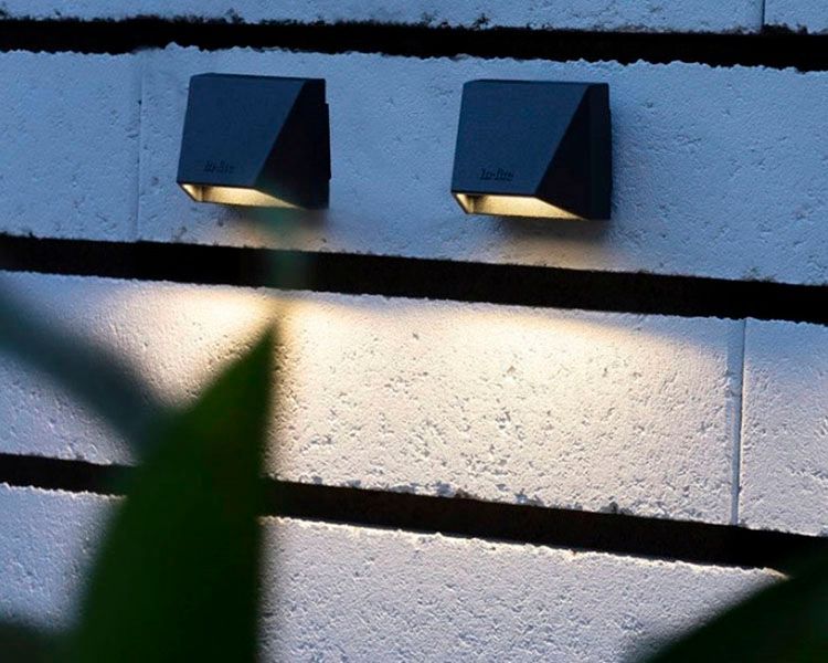 Two small black wall lights casting warm light on a white brick wall at dusk.