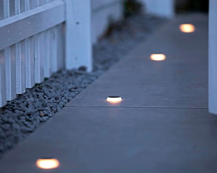 Outdoor walkway with small glowing ground lights beside a white railing at dusk