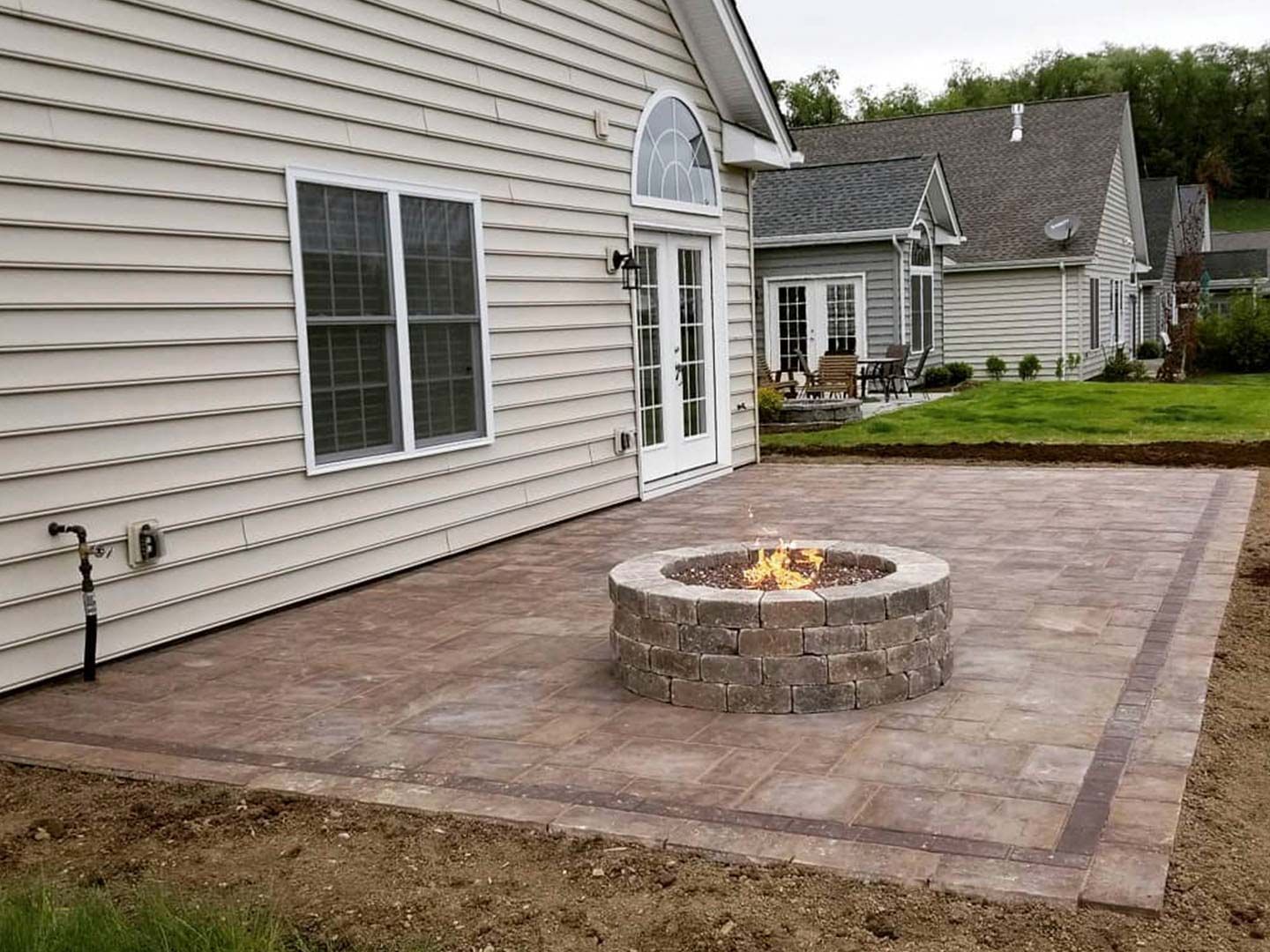 Stone patio with a round fire pit beside a house and white sliding door