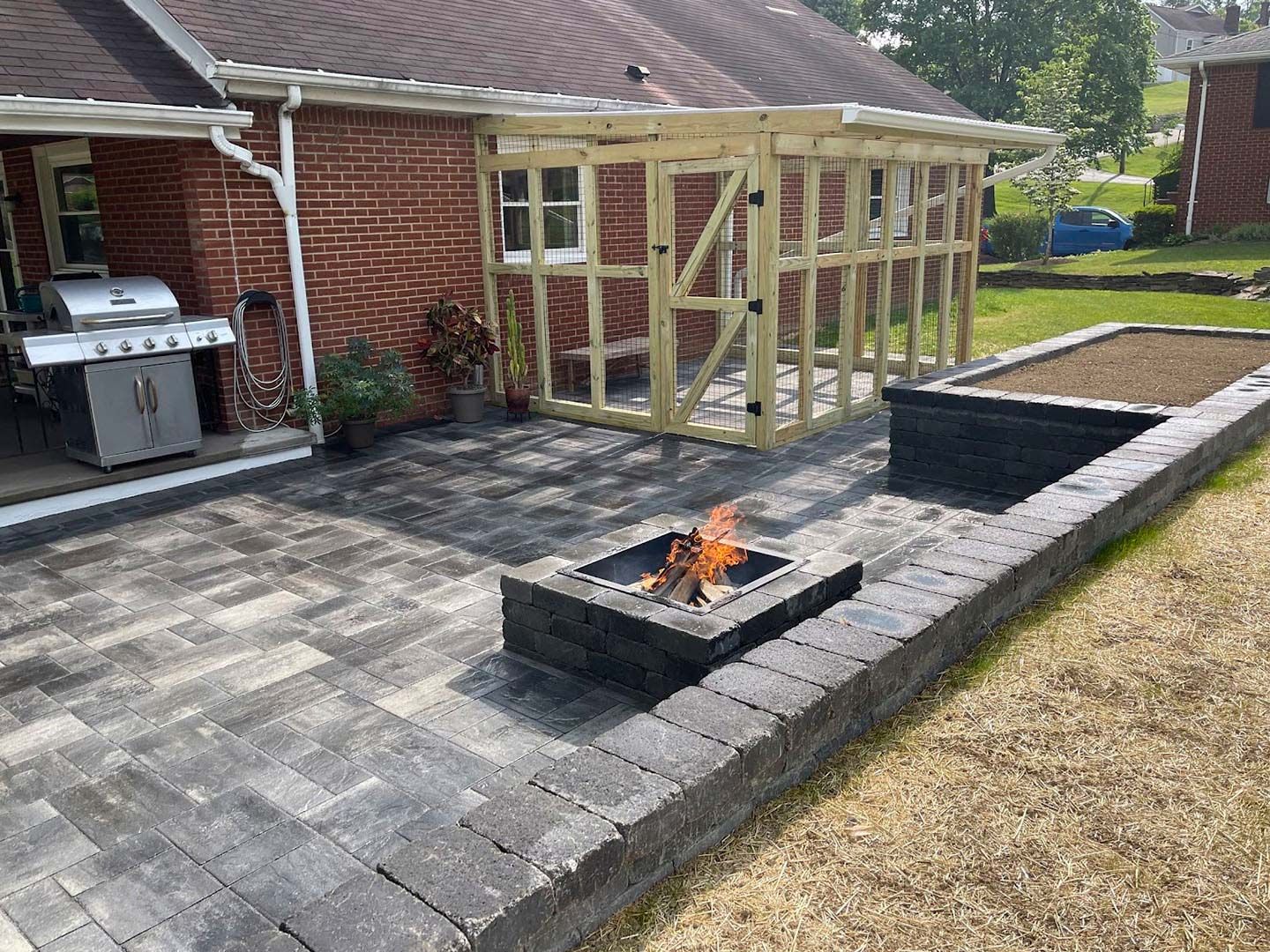 Backyard patio with a fire pit, paver seating area, and a partially framed garden structure beside a brick house